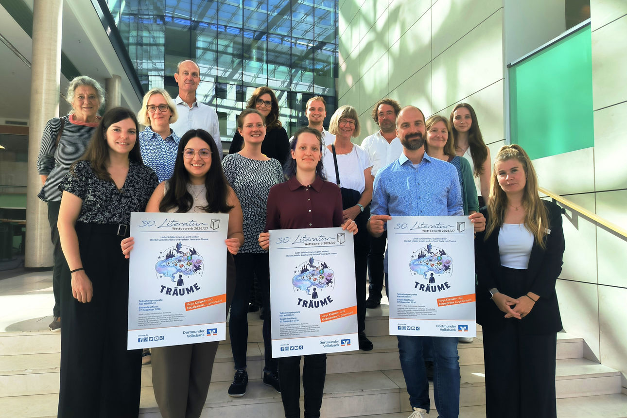 Eine Grupe steht zusammen und hält drei Plakate mit Werbung des Literaturwettbewerbs 