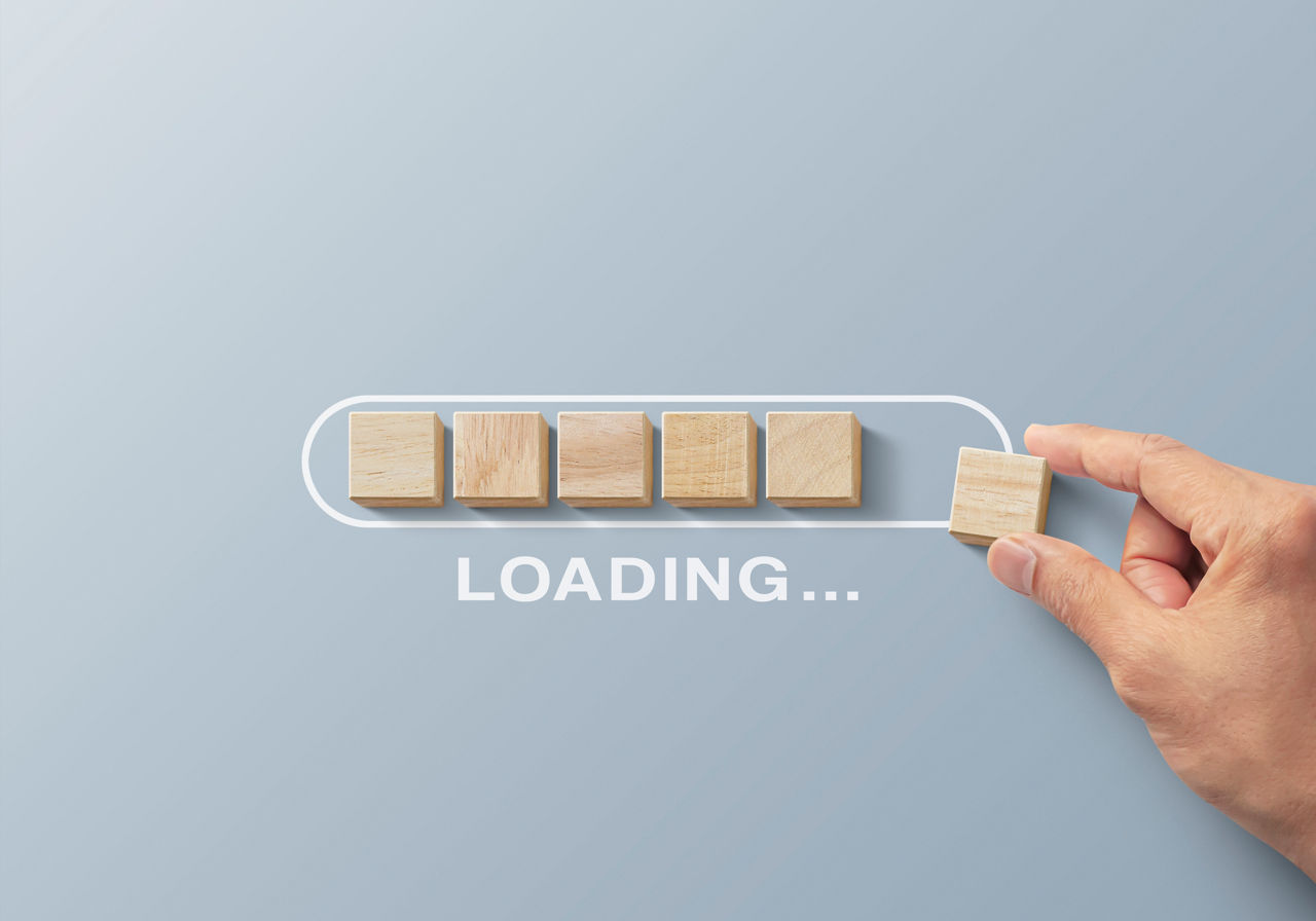 Loading, reboot, refresh or mindset concept. Hand putting wooden blocks in progress bar on gray background with the word LOADING.