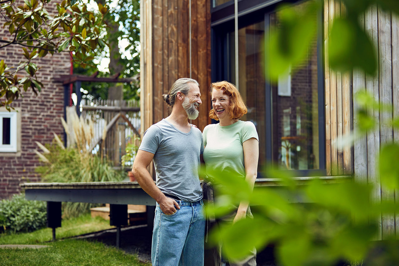 Ein lächelndes Paar steht im Garten vor einem modernen Holzhaus.