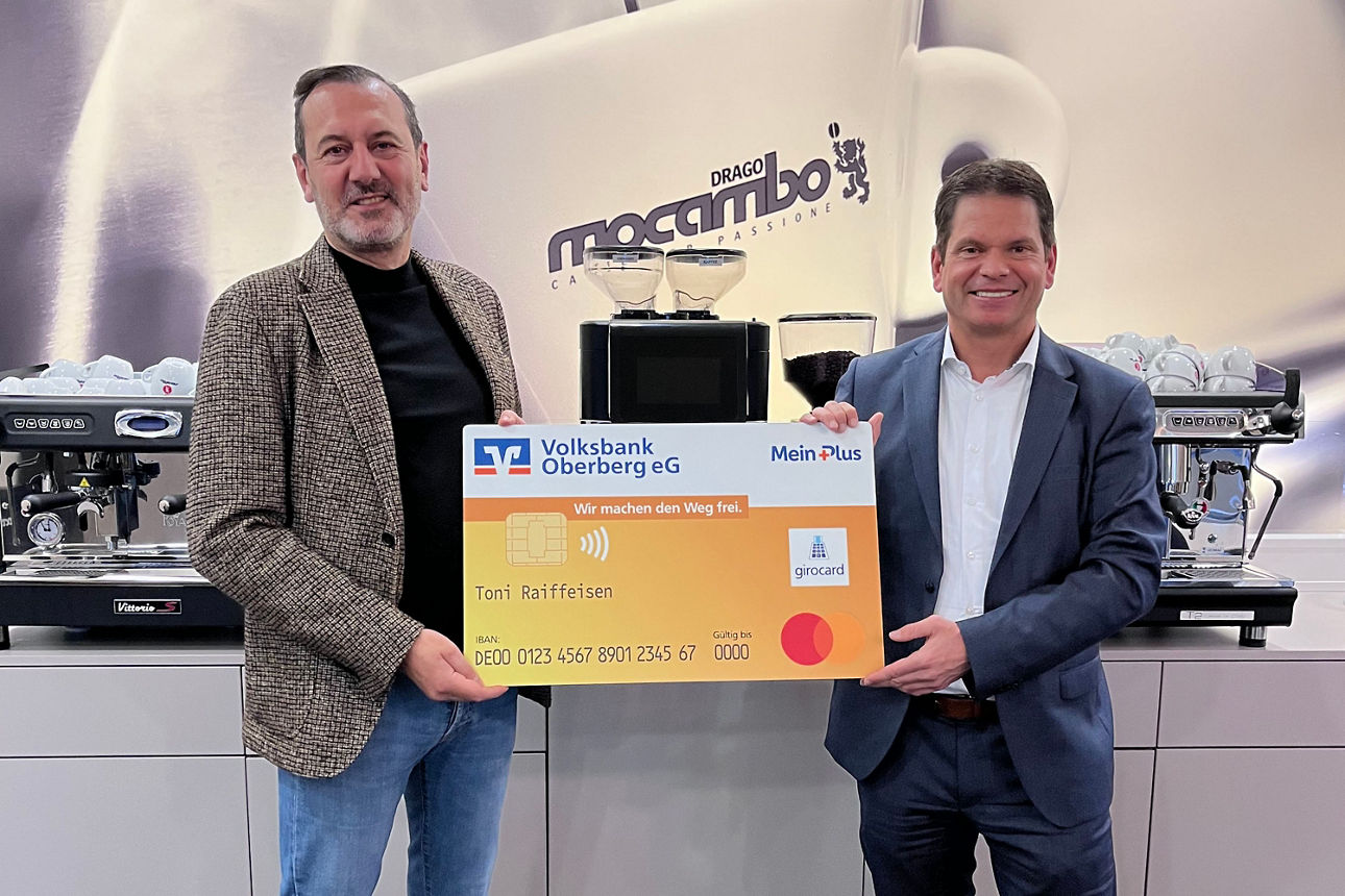 Zwei Männer in die Kamera und halten gemeinsam eine übergroße, symbolische Bankkarte der Volksbank Oberberg.