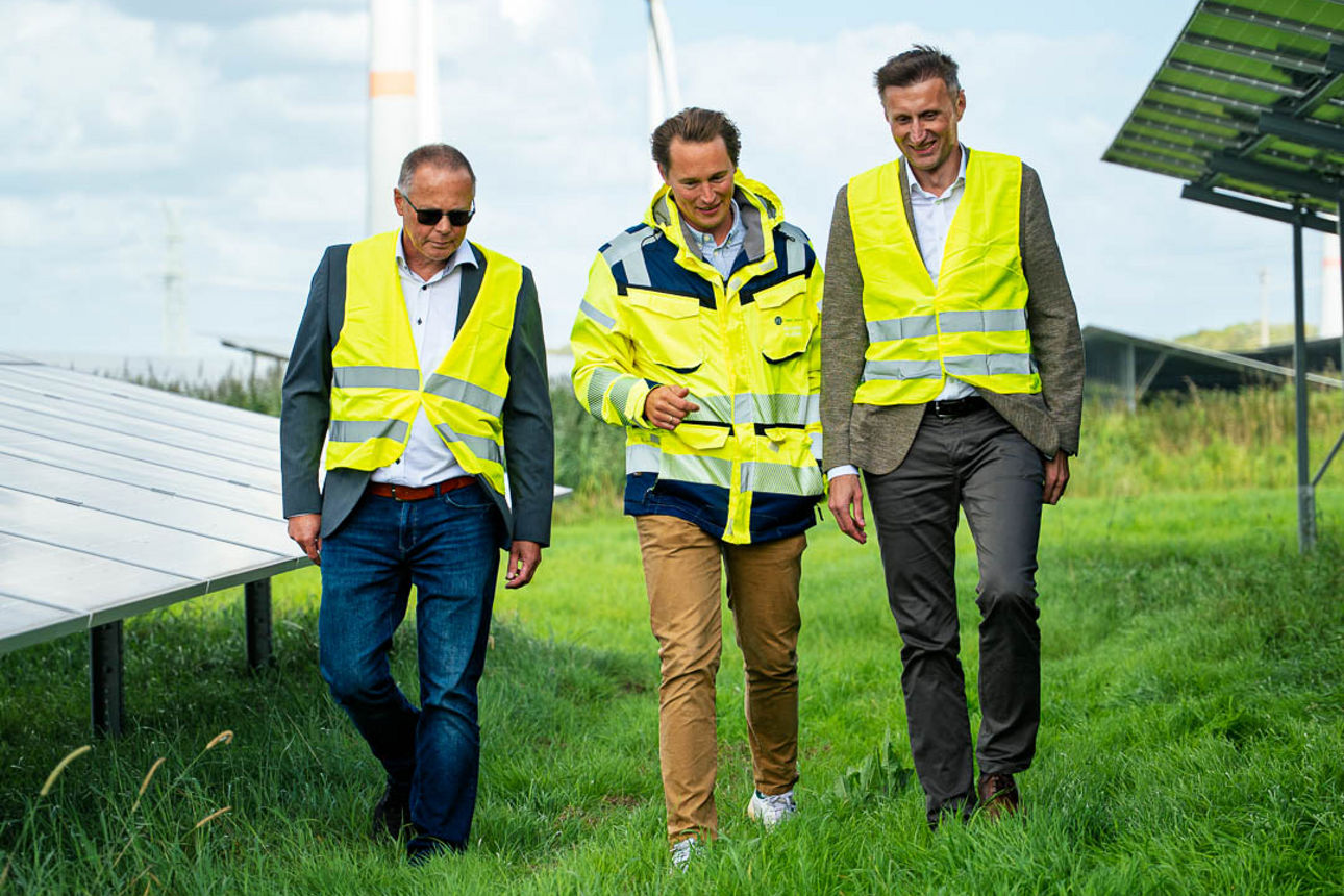 Drei Personen im Solarpark mit Windrädern im Hintergrund