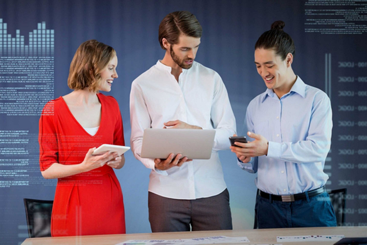 Drei Personen stehen vor digitaler Textwand mit Laptop in der Hand