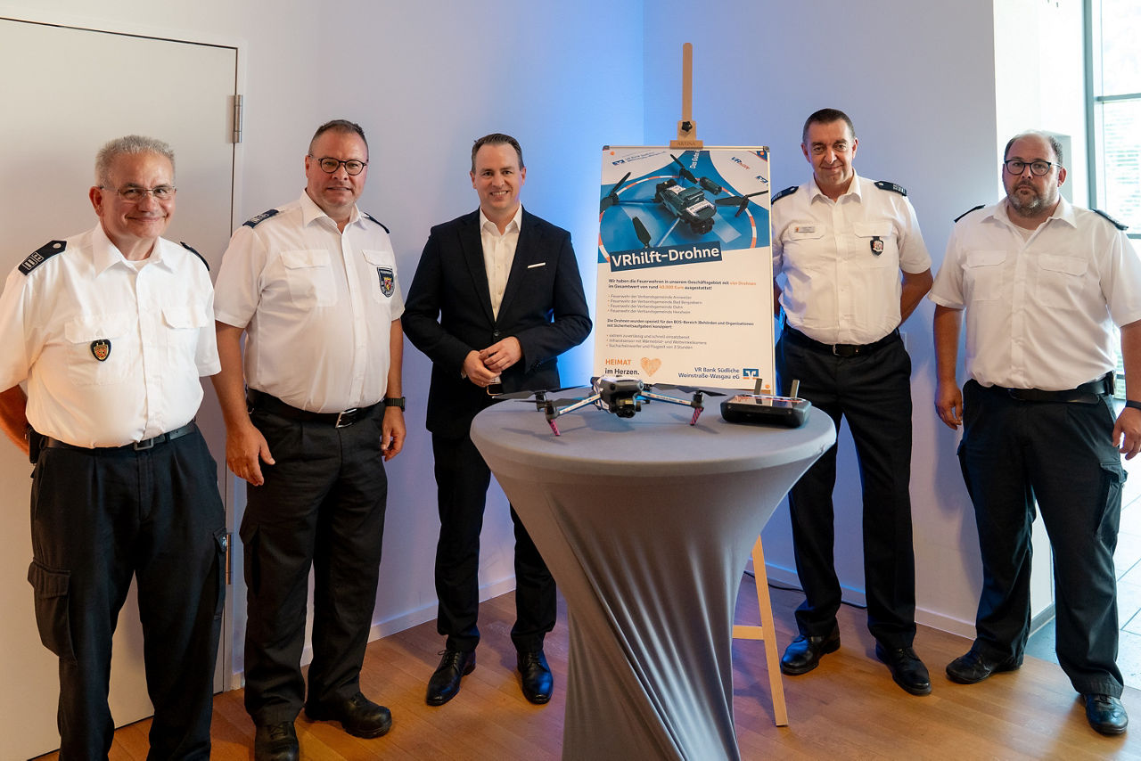  Feuerwehrmänner und ein Mann im Anzug um einen Stehtisch stehend.
