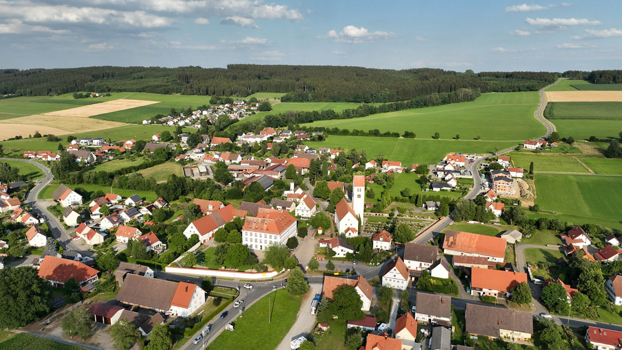 Luftaufnahme von Haisterkirch mit Kirche, Wohnhäusern, Straßen sowie weitläufigen Feldern und Wäldern in der Umgebung.