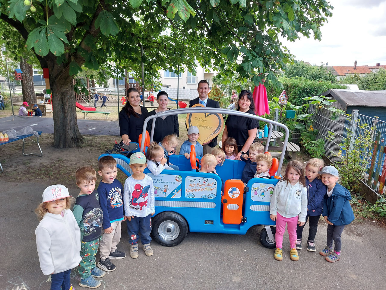 Kindergartenkinder mit ihren Erzieherinnen vor einem elektr. Kinderbus
