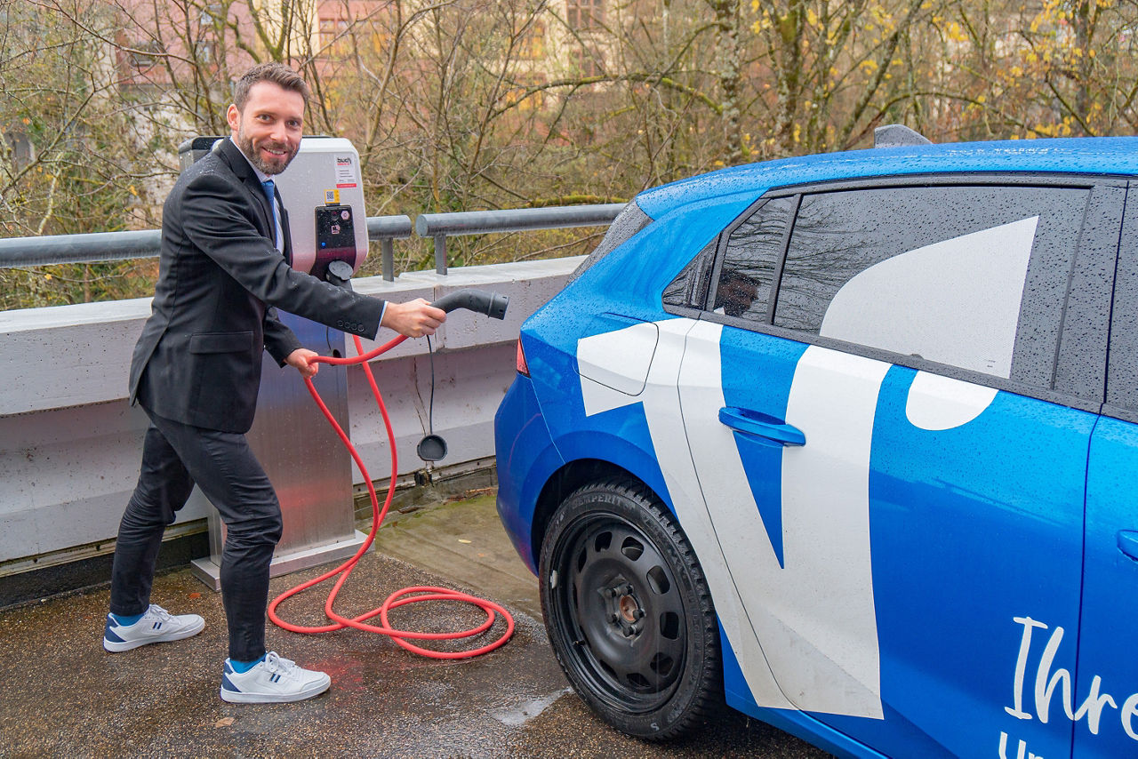 Ein Mitarbeiter der Volksbank Hochrhein hat ein Ladekabel für ein E-Auto in der Hand. Die E-Ladesäule auf dem Parkplatz.