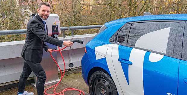 Ein Mann, der gerade an einer E-Ladesäule mit seinem Auto steht und das Auto auflädt.