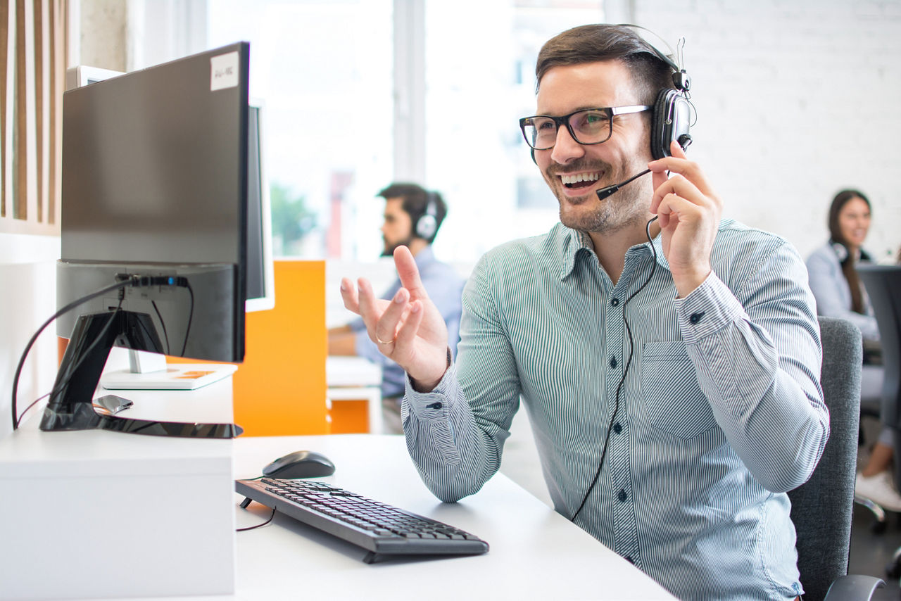 Fröhlicher, gutaussehender Technischer Support-Mitarbeiter mit Headset, der in einem Callcenter arbeitet.