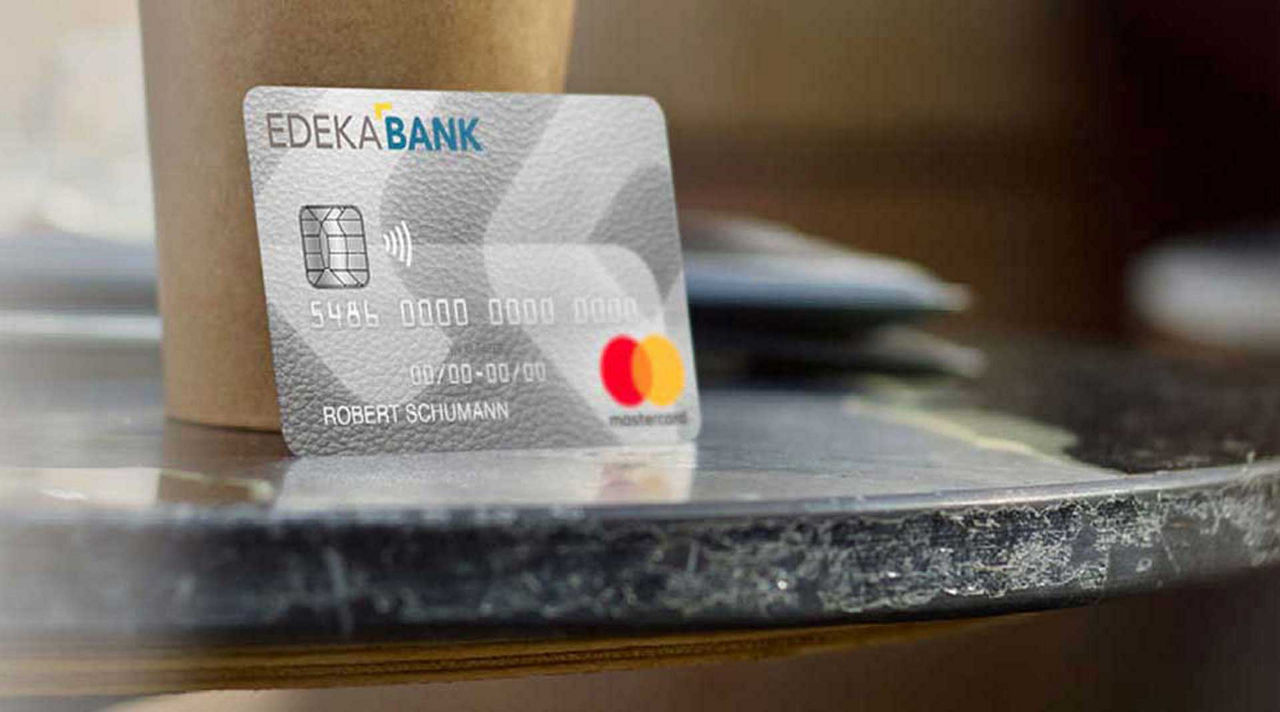 Die EDEKA-Mastercard® Classic steht angelehnt an einem Pappbecher