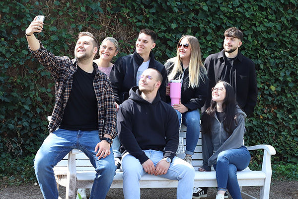 EIne Gruppe von Kollginnen und Kollegen sitzen auf einer Parkbank und machen ein Selfie