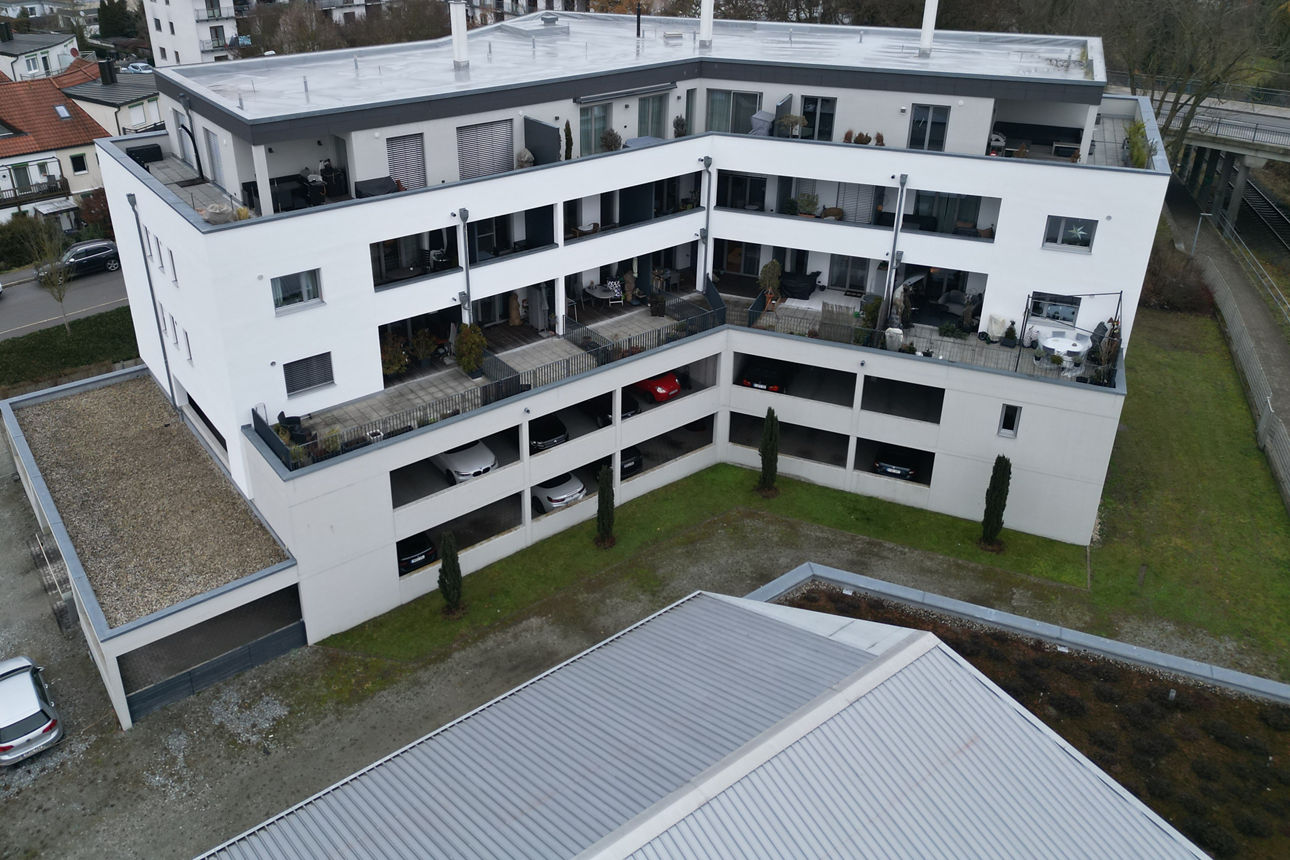 Auf dem Bild ist ein weißer Wohnblock zu sehen der aus der Drohnenperspektive fotografiert wurde. 