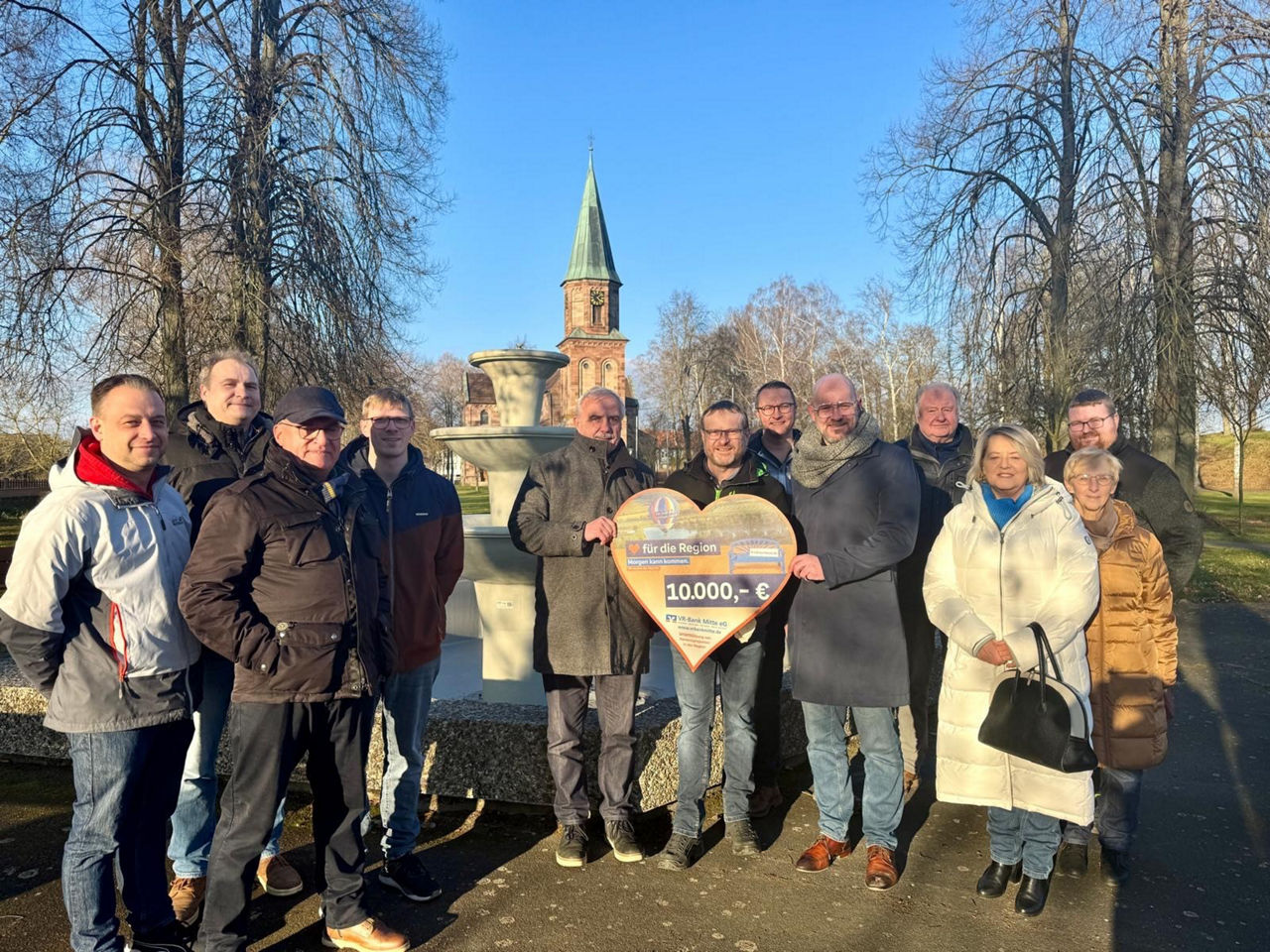 Menschengruppe steht vor dem Brunnen in Germershausen und bekommt den Scheck für die Spendenübergabe