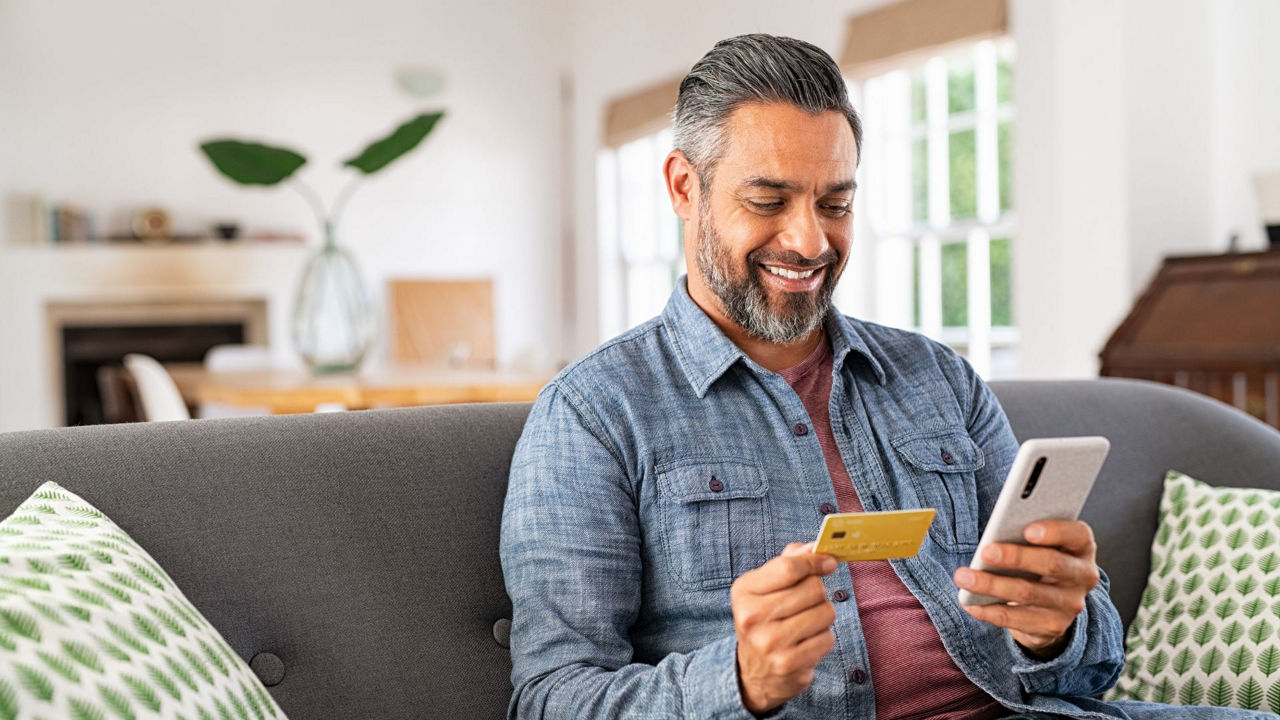 Ein Mann sitzt auf der Couch und hat eine Bankkarte und ein Handy in der Hand