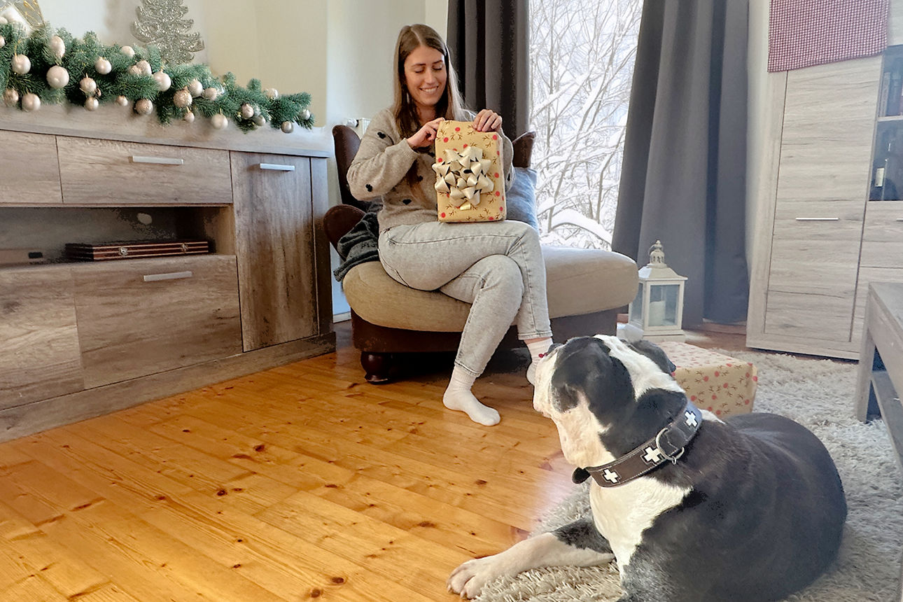 Eine Person sitzt im weihnachtlich dekorierten Wohnzimmer mit einem Geschenk