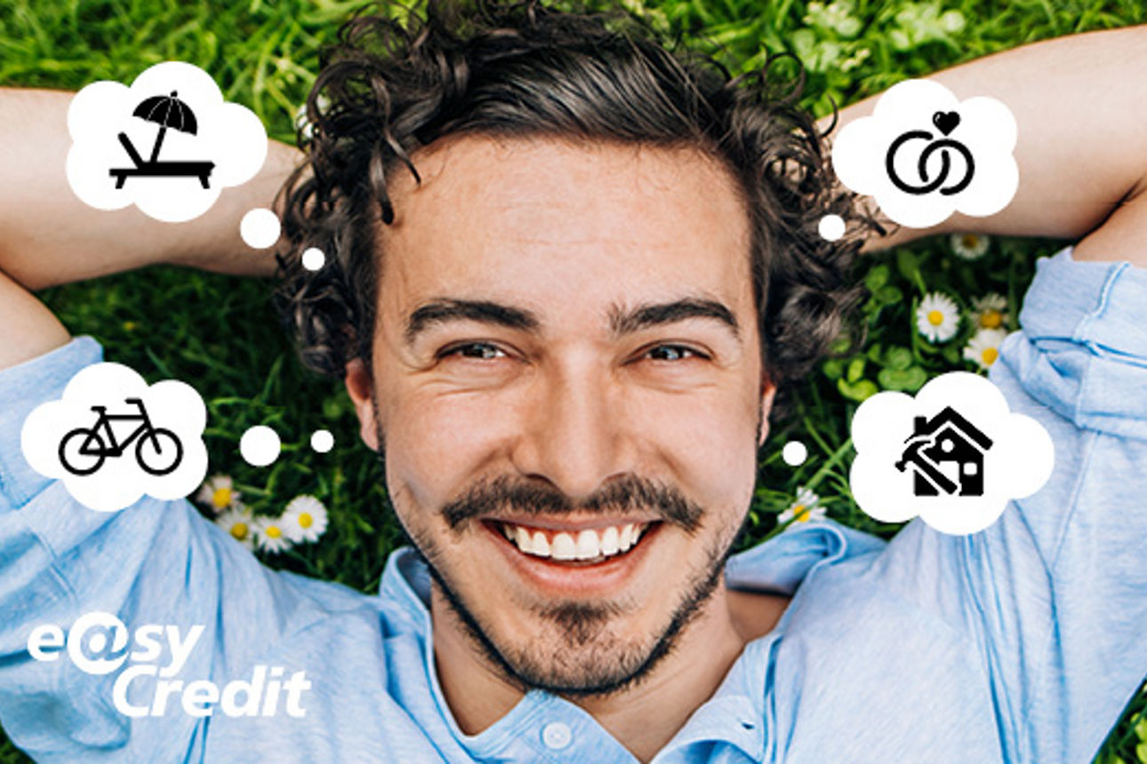 Ein lächelnder Mann liegt auf dem Rücken auf einer Wiese mit den Händen hinter dem Kopf verschränkt. 