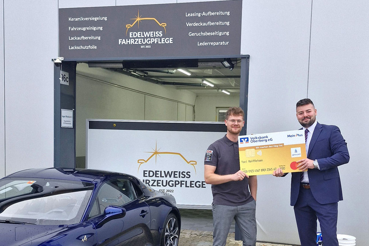 Zwei Männer in die Kamera und halten gemeinsam eine übergroße, symbolische Bankkarte der Volksbank Oberberg.