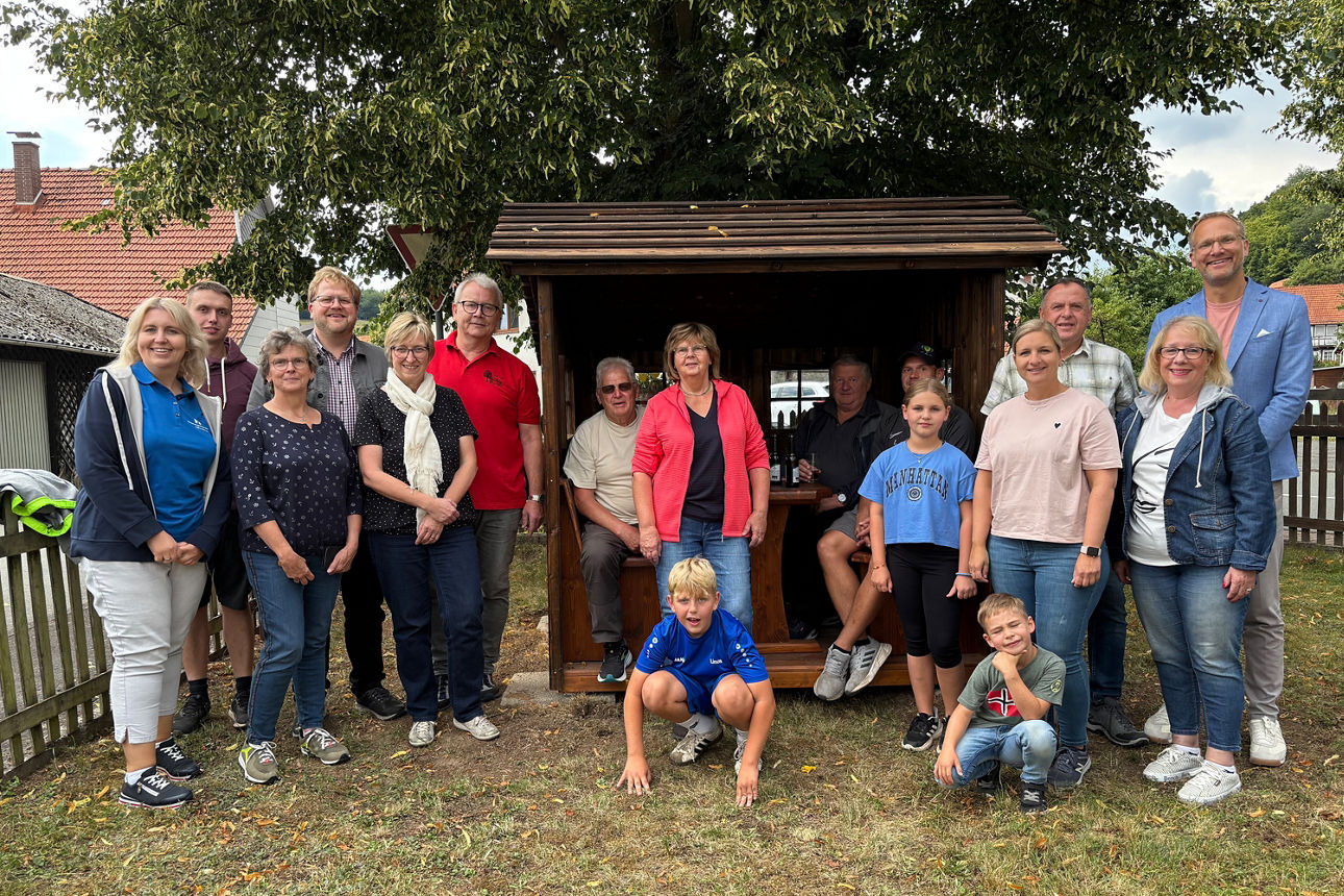 eine große Gruppe von Menschen unterschiedlichen Alters zu sehen, die sich für ein Foto vor und in einer hölzernen Schutzhütt