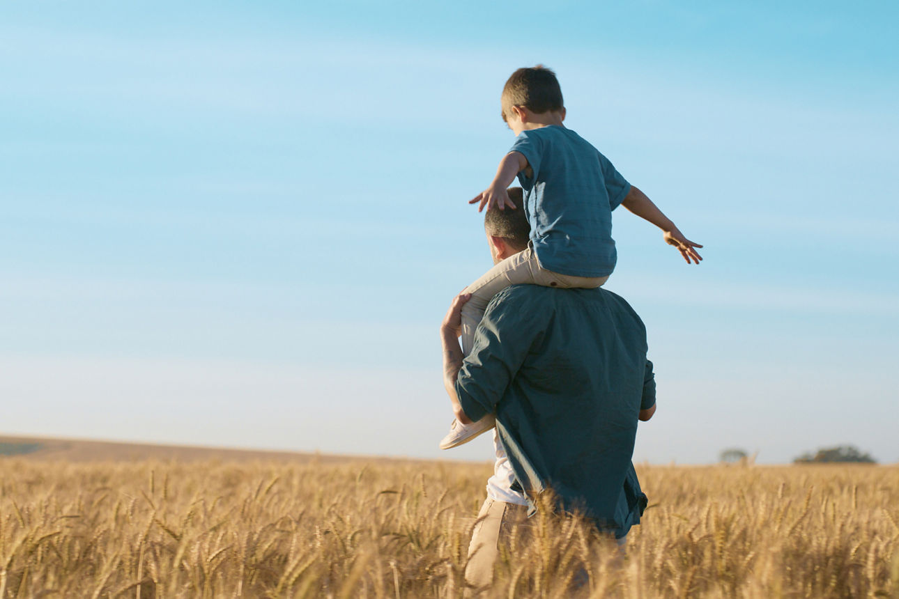 Vater spaziert mit seinem Sohn auf den Schultern über ein Feld