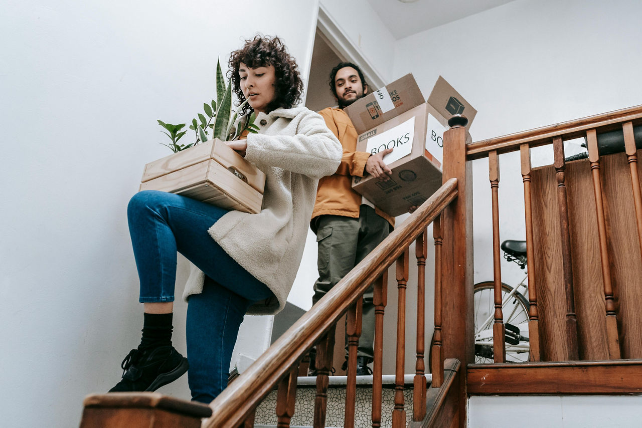 Ein Mann und eine Frau tragen Umzugskartons eine Holztreppe herunter