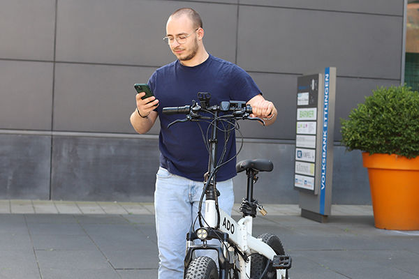 Ein Mitarbeiter schiebt sein Fahrrad durch den Hof und schaut aufs Handy