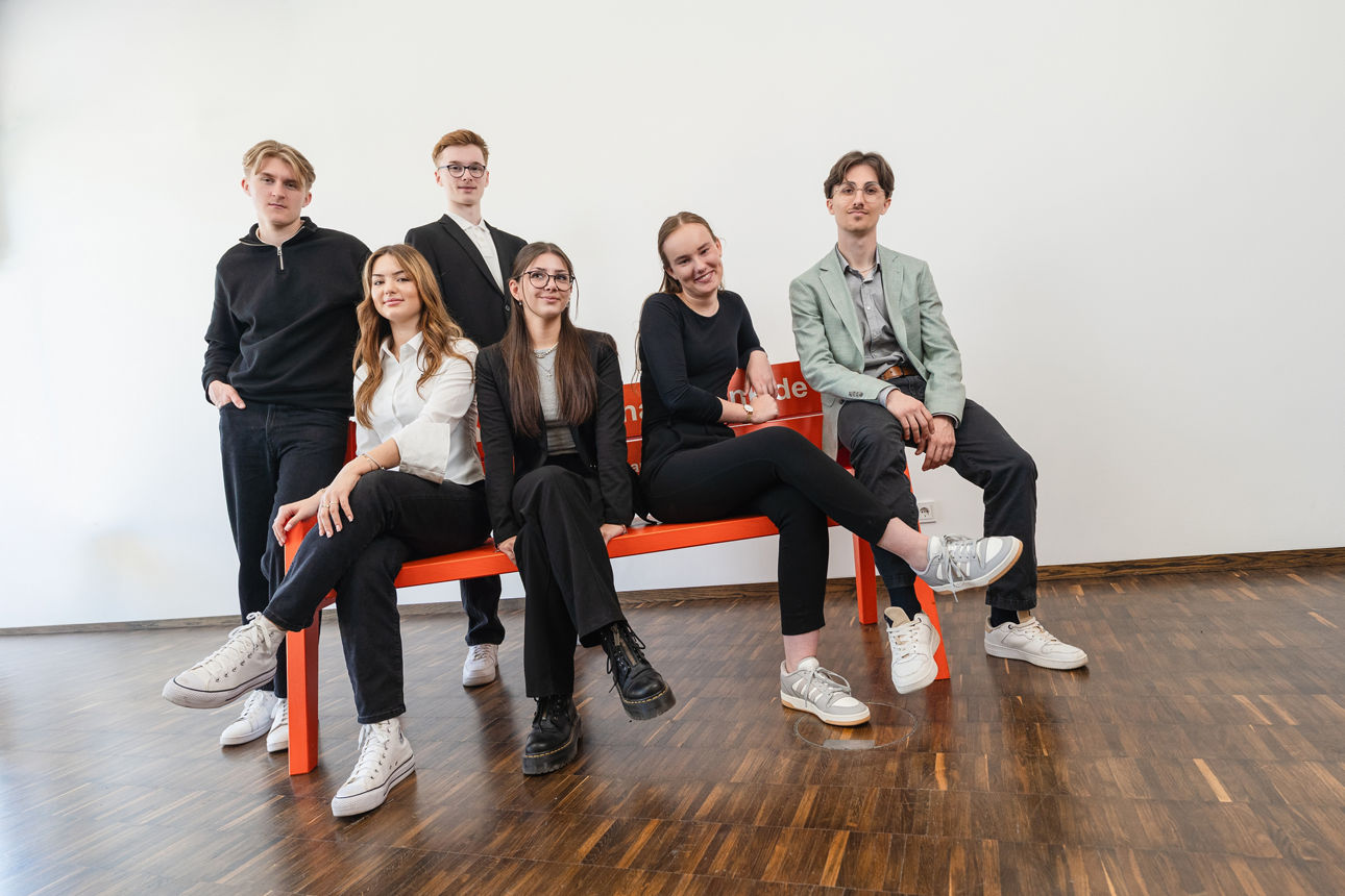 Eine Gruppe von jungen Leuten sitzt auf einer orangenen Bank
