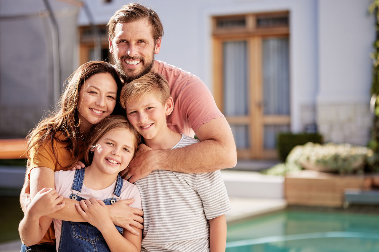 Eine Familie, bestehend aus vier Personen zwei Erwachsene und zwei Kinder. Sie stehen im Freien vor einem modernen Haus.