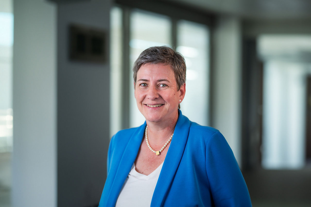 Eine lächelnde Dame mit blauem Blazer steht im Raum