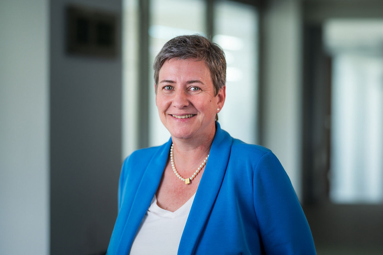 Eine lächelnde Dame mit blauem Blazer steht im Raum