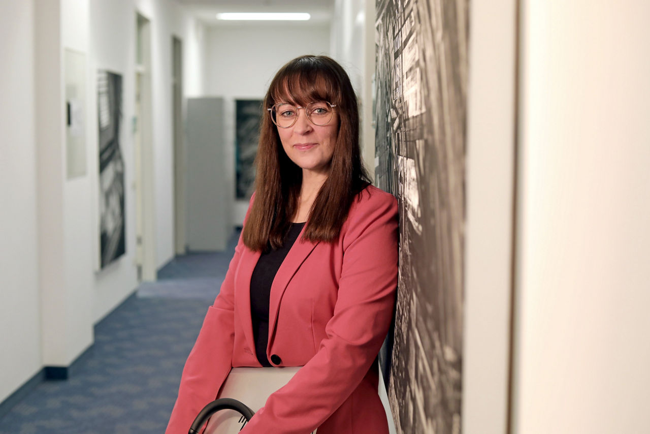 Mitarbeiterin der Bank, Susanne Eisenmann, lehnt an Wand und lächelt in die Kamera