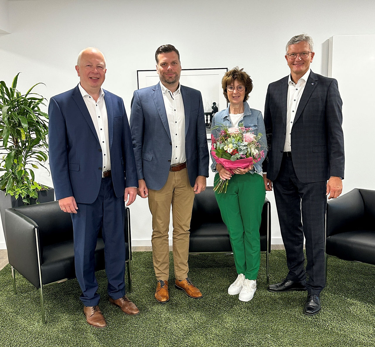 Drei Männer und eine Frau stehen nebeneinander. Die Frau hat einen Blumenstrauß