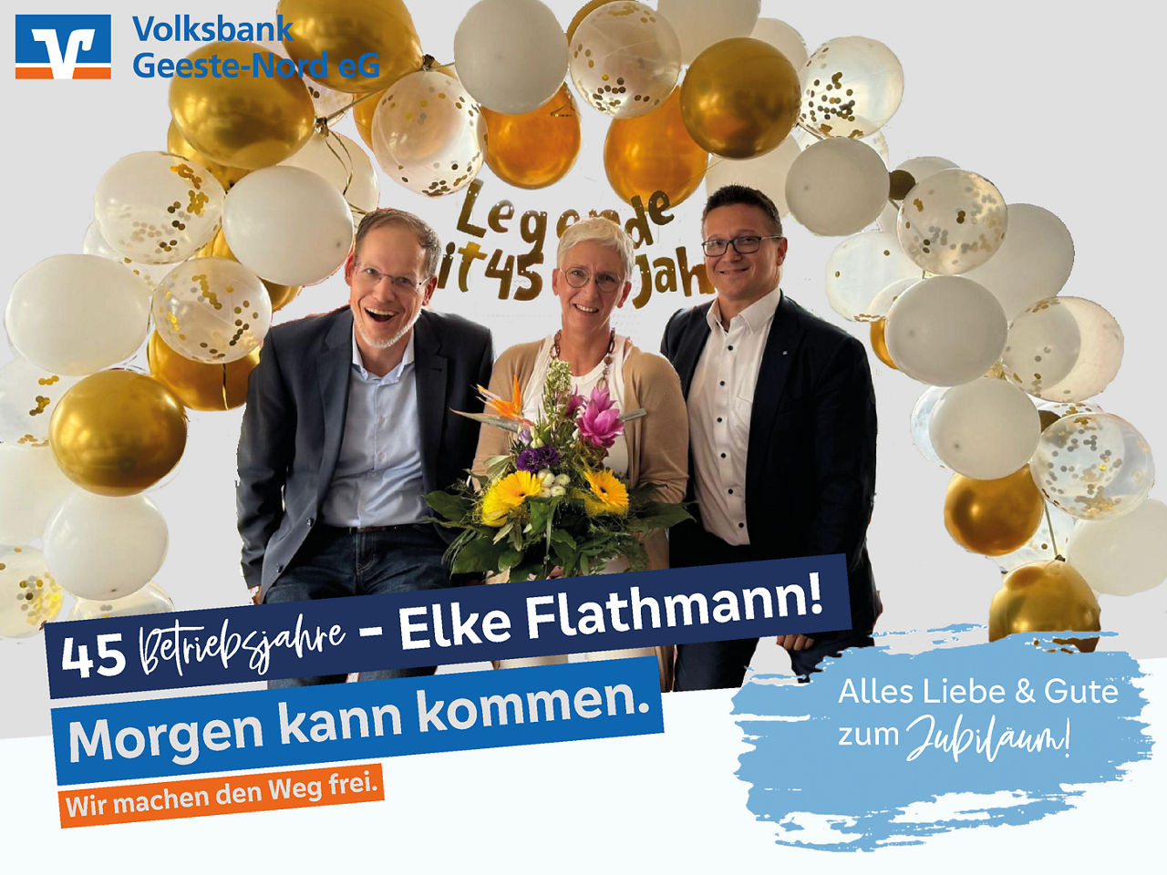 Vorstand und Mitarbeiterin unter einem Luftballonbogen