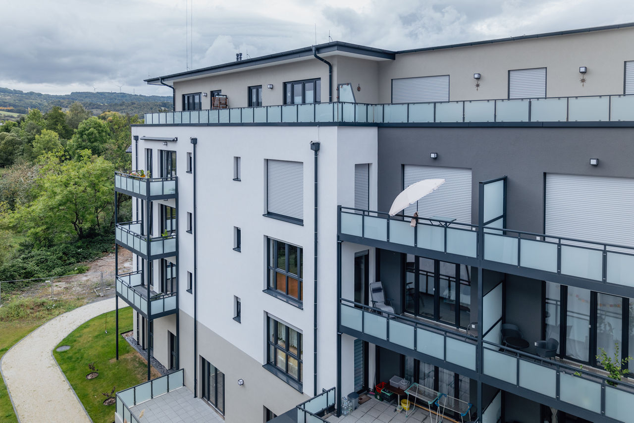 Schrägansicht eines mehrgeschossigen Wohngebäudes des Projekts ELMLAND1 mit umlaufenden Balkonen, großen Fensterflächen und moderner Fassadengestaltung. Die Aufnahme zeigt den fertiggestellten Baukörper im Zusammenspiel mit der umgebenden Grünanlage.