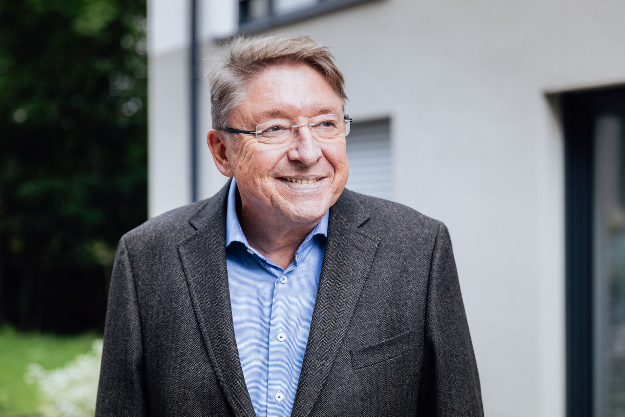 Eine Person steht im Außenbereich eines Wohngebäudes des Projekts ELMLAND1. Im Hintergrund sind Fassadenelemente und Fensterflächen sichtbar, die die moderne Gestaltung und den hochwertigen Ausbau des Projekts zeigen.