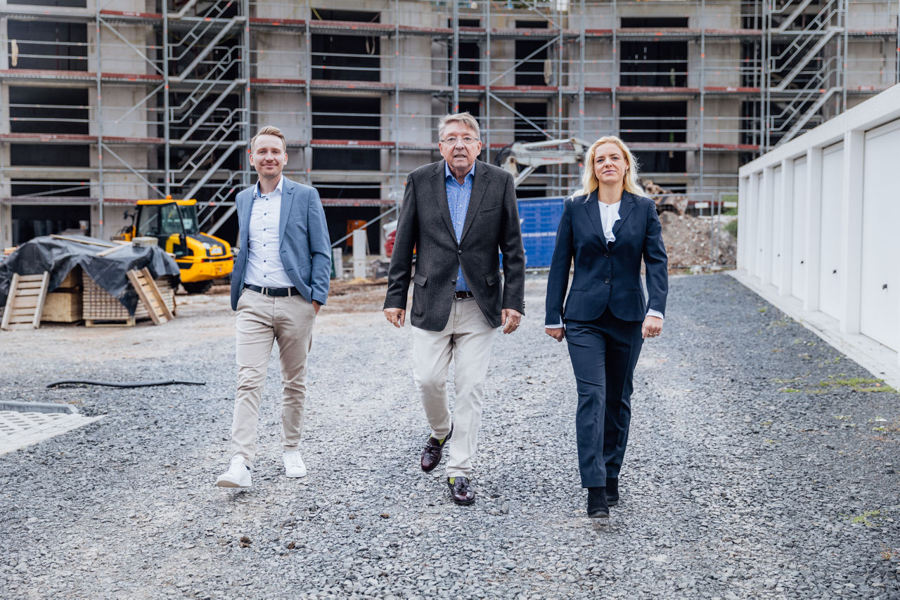Mehrere Personen bewegen sich über eine Baustellenfläche innerhalb des Wohnprojekts ELMLAND1. Im Hintergrund sind Gerüste, Baugeräte und ein im Ausbau befindliches Gebäude zu sehen, die den aktuellen Stand der Projektentwicklung dokumentieren.