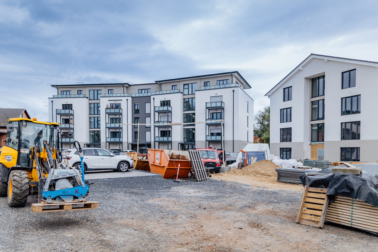 Blick auf den Außenbereich eines Wohnbauprojekts von ELMLAND1 während der Bauphase. Zu sehen sind mehrgeschossige Wohngebäude, Baugeräte, Materiallagerung und befestigte Flächen, die den aktuellen Stand der Projektentwicklung dokumentieren.
