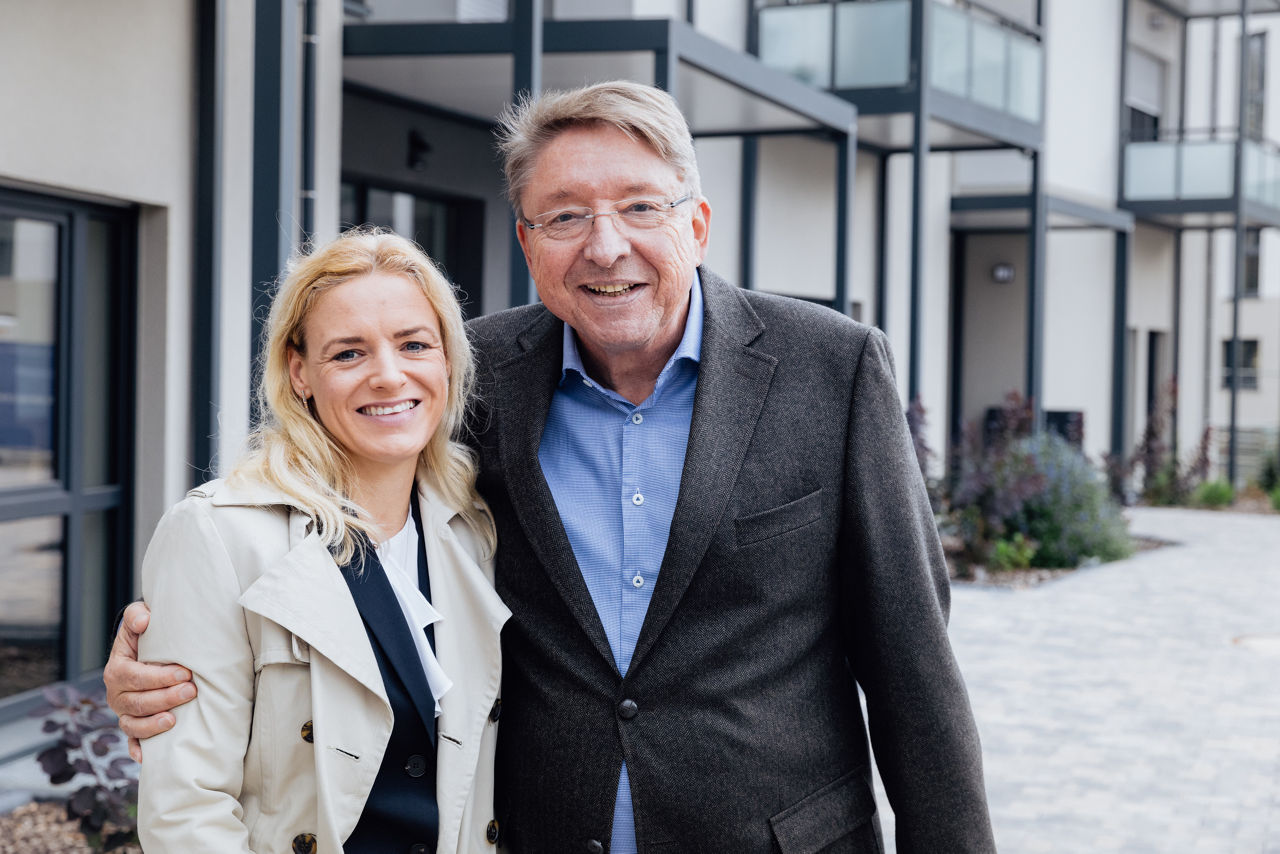 Zwei lächelnde Personen stehen vor einem modernen Wohngebäude