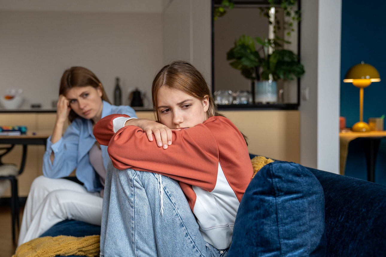 Eine frustierte Jugendliche sitzt vor der Kamera, ihre verzweifelte Mutter ist im Hintergrund zu sehen.