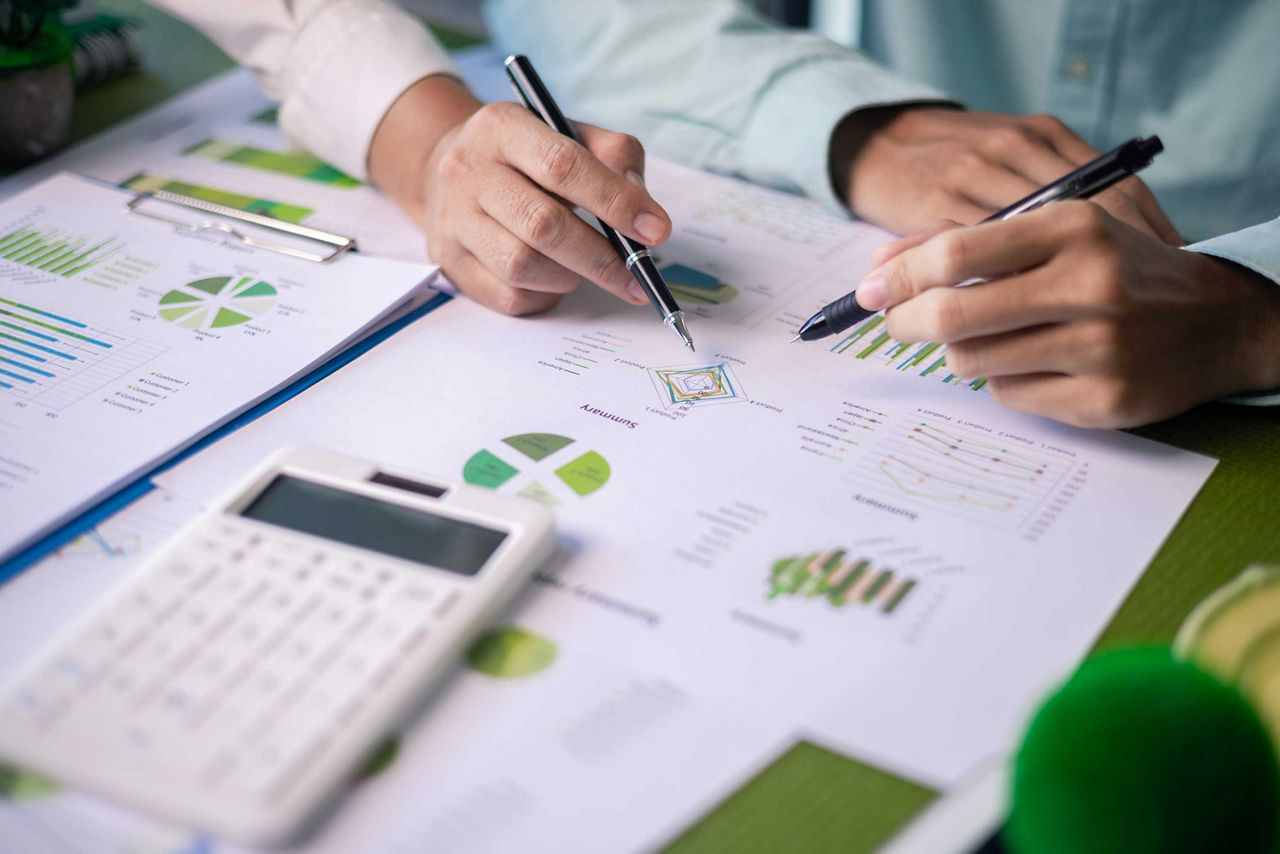 Diverse Zettel mit Tabellen und Diagrammen werden mit Stift und Taschenrechner besprochen