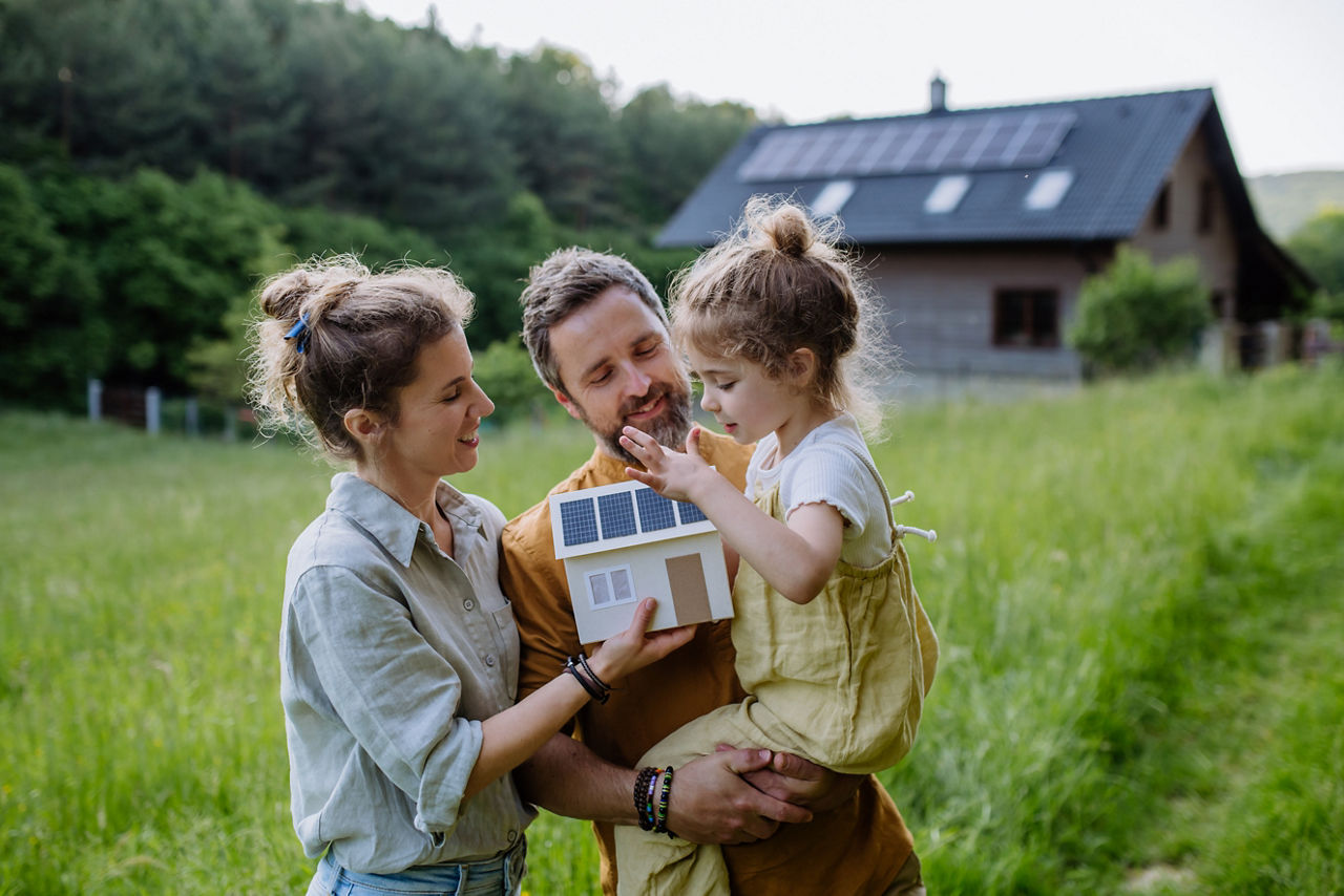 Dreiköpfige Familie steht auf der Wiese vor einem Einfamilienhaus mit Solarpanelen
