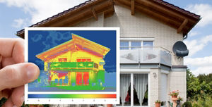 Eine Person hält ein Thermografie-Bild vor ein modernes Einfamilienhaus. Das Thermografie-Bild zeigt Temperaturunterschiede
