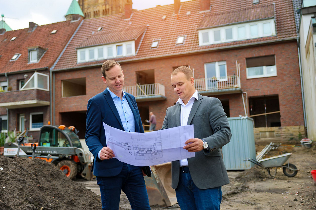 Energieberater Michael Vettel und Gerrit Schöpper mit Bauplan vor einem Bauprojekt