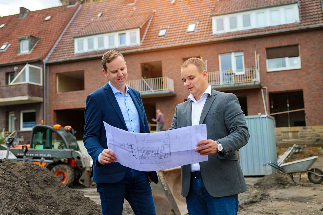 Energieberater Michael Vettel und Gerrit Schöpper mit Bauplan vor einem Bauprojekt