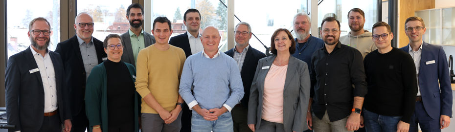Gruppenfoto von 14 Personen bei einem Netzwerktreffen in heller Umgebung mit Fenstern. Es handelt sich um die Mitglieder des Energienetzwerks.