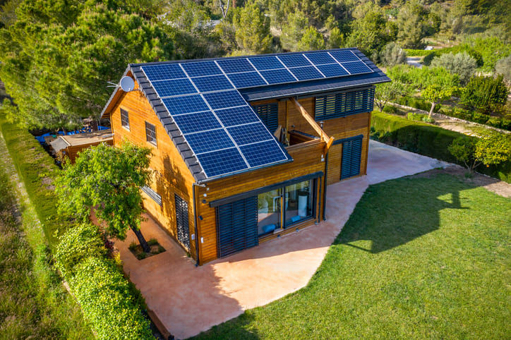 Bild eines Holzhauses im Grünen mit einer PV-Anlage auf dem Dach