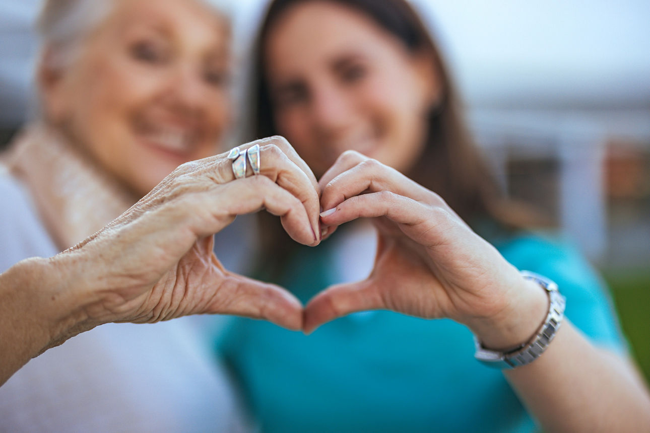 Engagement - zwei Frauen formen mit ihren Händen ein Herz, die Gesichter im Hintergrund sind verschwommen