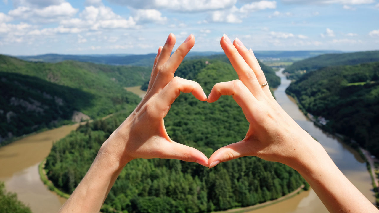Hände-Herz-Geste gegen panoramische Sommeransicht der Saarschleife im Saarland.