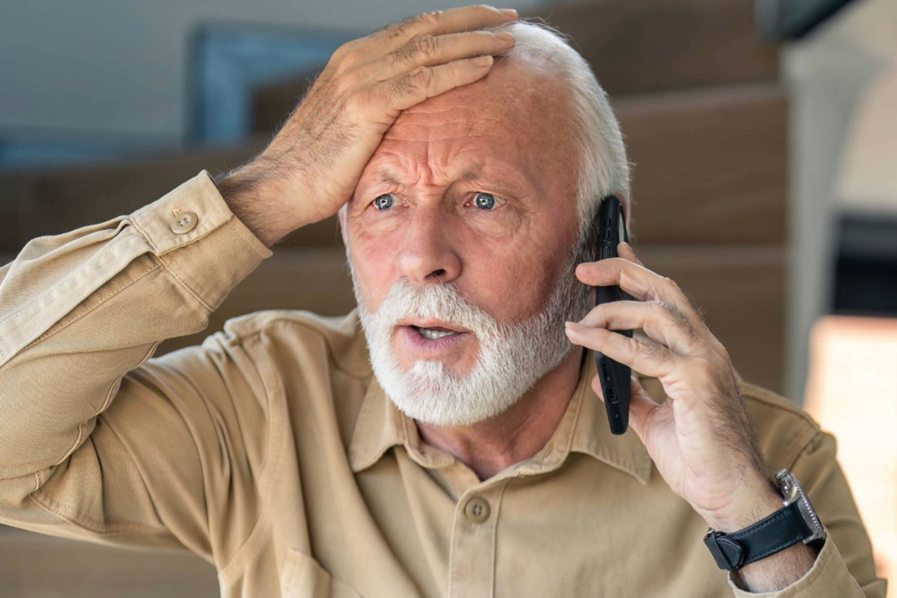 Ein älterer Mann telefoniert und fasst sich erschrocken an die Stirn.