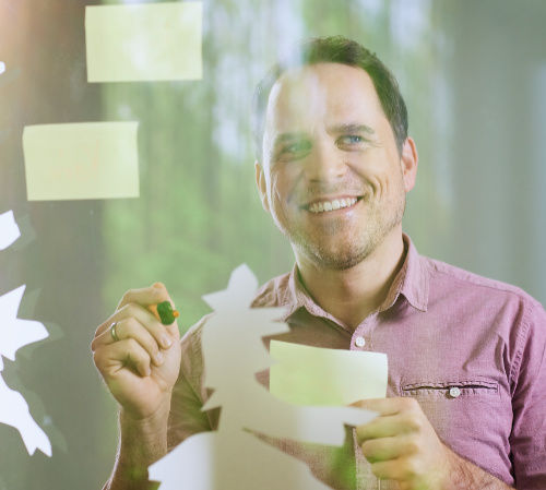 Mann steht hinter Galswand an der Post-Its hängen