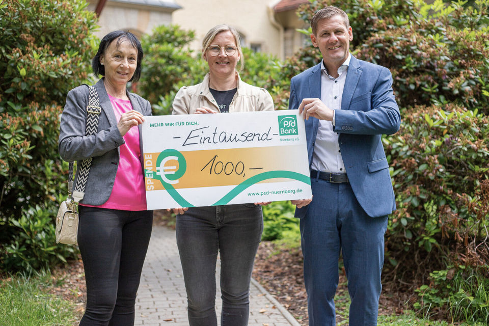 Zwei Kolleg:innen der PSD Bank Nürnberg überreichen dem Epilepsiezentrum Kleinwach einen den Spendencheck in Höhe von 1.000€.