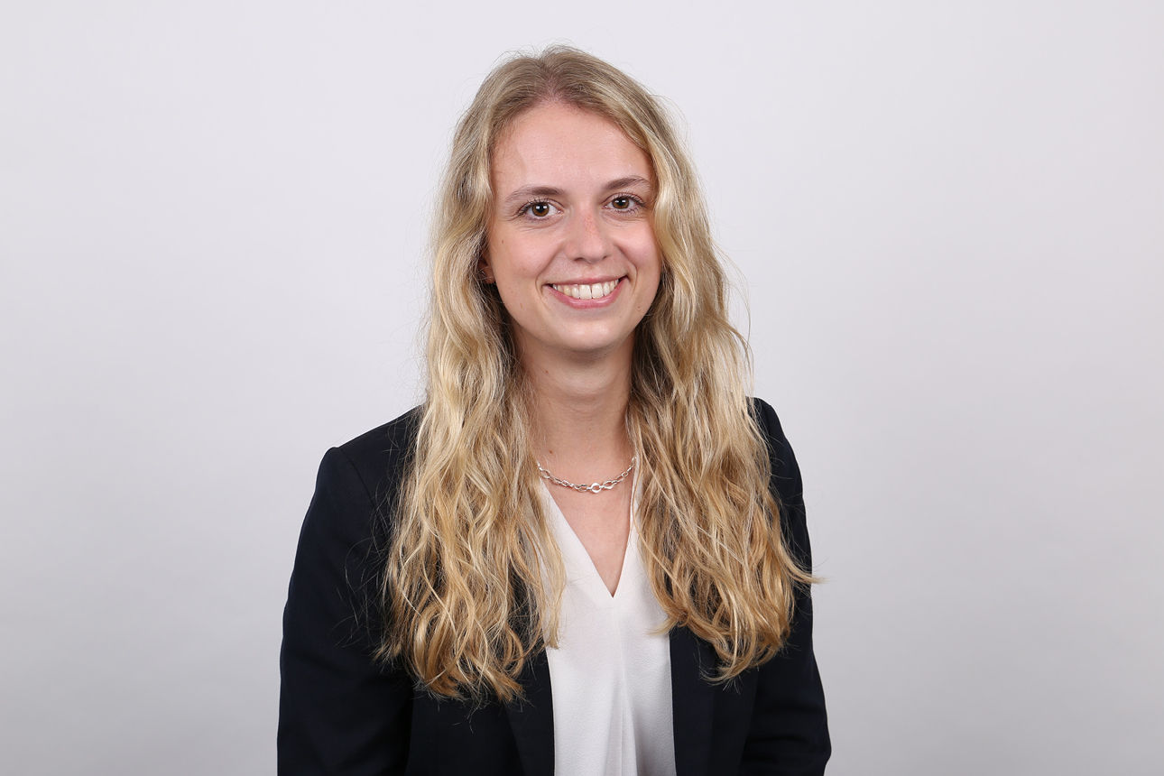 Mitarbeiterin vor weißem Hintergrund lächelt in die Kamera